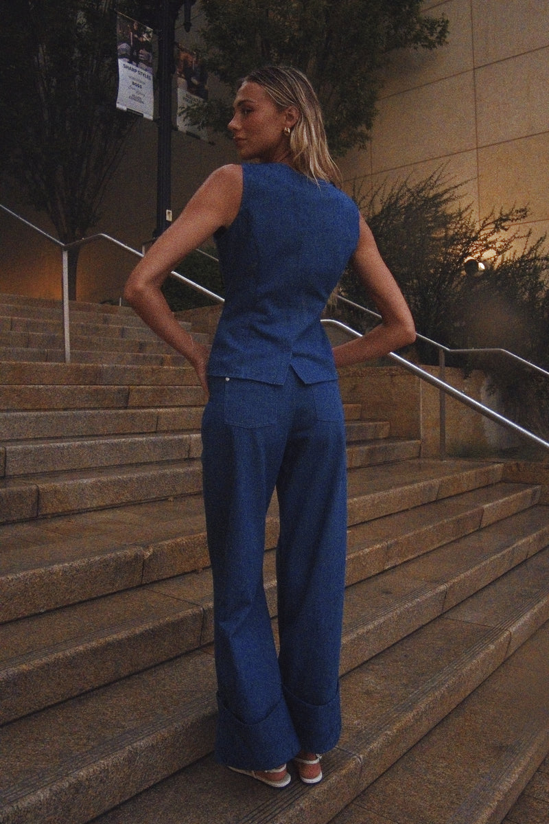 A woman stands on outdoor stone stairs wearing a matching blue sleeveless top and wide-leg pants set, photographed from the back.